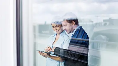 Colleagues dressed in business attire interacting with a tablet.